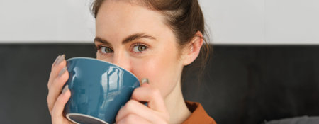 Close up portrait of beautiful, relaxed young woman, enjoying aroma of coffee, drinking cappuccino...