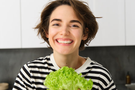 Close up portrait of beautiful, healthy smiling woman, posing with green lettuce leaf, cooking diet meal, preparing vegetarian salad, looking happyの写真素材