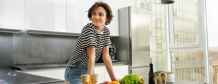 Portrait of happy, healthy young woman, vegetarian making herself salad, posing near vegetables on kitchen, chopping ingredients for vegan mealの写真素材
