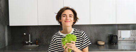 Portrait of happy and healthy young woman, following her diet, posing with lettuce leaf and smiling, cooking in the kitchen, vegetarian loves her vegetablesの写真素材