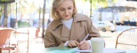 Portrait of carefree, blond cute woman working with documents, drinking takeaway coffee and sitting...