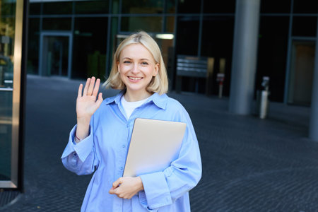 Friendly smiling student, blond girl with notebooks, tutor waving hand at camera, saying hello,...