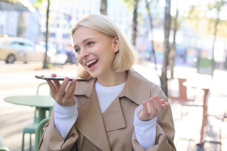 Close up portrait of young smiling woman, lively recording voice message, talking into smartphone...