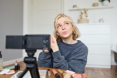 Portrait of young creative social media content creator, woman showing lipstick swatches on her hand, recording video about beauty and makeup, sitting in her room in front of digital cameraの写真素材