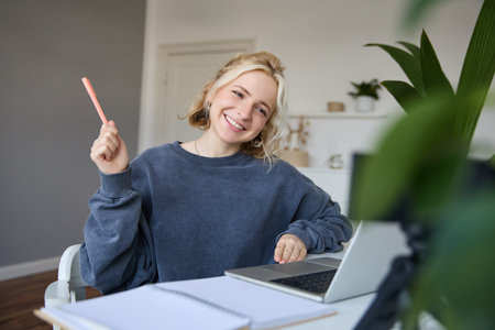 Portrait of young smiling woman, student talking to teacher online via video chat, doing course, attends remote course in internet, making notesの写真素材