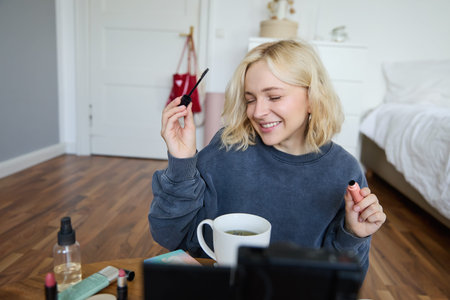 Young charismatic beauty blogger, teenage girl records video of her applying mascara, reviewing...