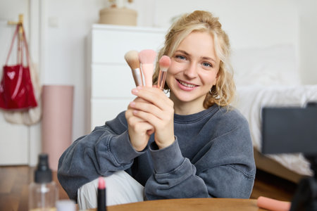 Portrait of content media creator, blogger sits in her room and records video of her favourite makeup brushes, talks on cameraの写真素材