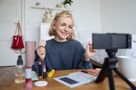 Portrait of young woman, beauty content creator, sitting in a room in front of digital camera, recording makeup tutorial vlog, showing cosmetic facial productsの写真素材