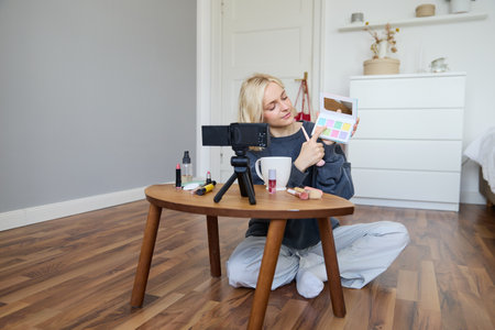 Portrait of beautiful lifestyle blogger, girl records a video on her camera for social media, shows palette of eyeshadows, does a makeup tutorial for her followers, sits in her roomの写真素材