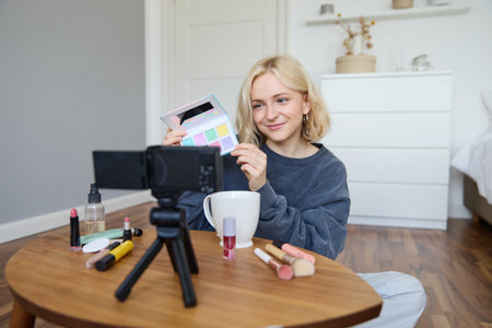 Lifestyle blogger, records video in her room, has a camera on coffee table, shows eyeshadow palette to her followers, does makeup tutorial, vlogger working indoors, creates content for social mediaの写真素材