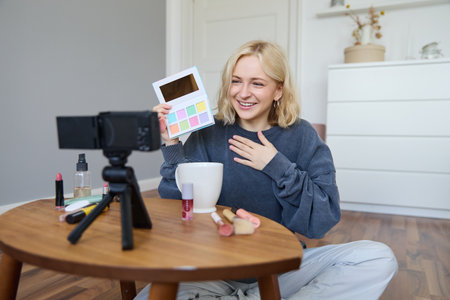 Portrait of beautiful smiling woman, recording video in her room, has camera on coffee table, reviewing makeup, doing lifestyle vlog for social media account, records a tutorialの写真素材