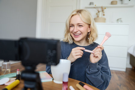 Close up portrait of happy young beauty blogger, records lifestyle vlog in her room, using camera with stabiliser, shows makeup brush and cosmeticsの写真素材