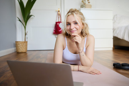 Portrait of young fitness woman, doing workout at home, looking at her gym instructor on laptop screen, doing online training sessionの写真素材