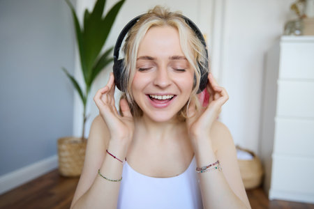 Close up portrait of woman smiling while listening to music in wireless headphones, singing with eyes closedの写真素材