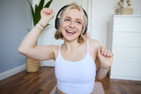 Portrait of charismatic, beautiful young woman dancing and listening to music in wireless headphones, singing along favourite song in her roomの写真素材