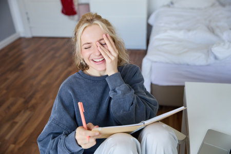 Portrait of charismatic blond girl, smiling woman in bedroom, holding notebook and pen, writing in journal or diary, creates to do list in plannerの写真素材