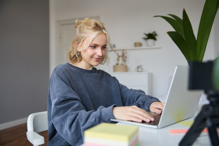 Portrait of young woman, student studying at home on remote education, working on laptop, typing on keyboardの写真素材