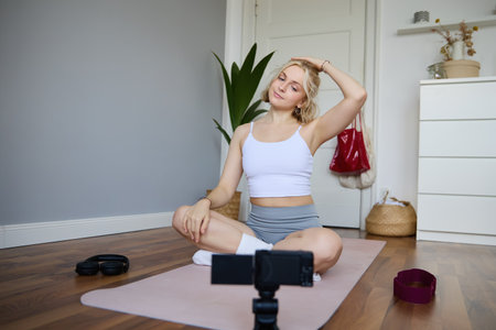 Portrait of young woman personal yoga instructor, recording workout video at home, using digital camera to vlog her exercises, using rubber matの写真素材