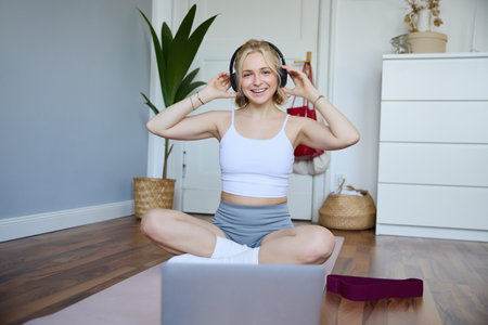 Portrait of fit and healthy young woman in wireless headphones, does workout, using online video tutorials, listens to fitness instructor on laptop, exercising at homeの写真素材