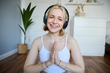 Portrait of young relaxed woman, sits in room in headphones, clasp hands together, meditated, listens to yoga musicの写真素材