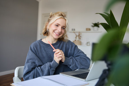 Portrait of young smiling woman, student talking to teacher online via video chat, doing course, attends remote course in internet, making notesの写真素材