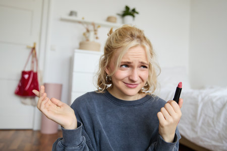 Portrait of woman, vlogger looking disappointed, showing lipstick and shrugging shoulders, recording video about makeup for social media accountの写真素材