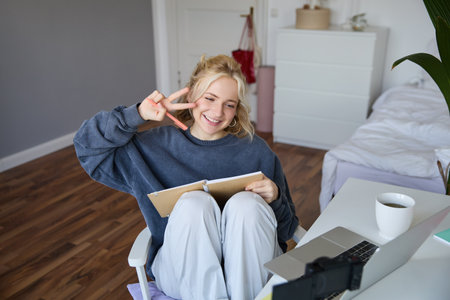 Portrait of smiling cute woman, lifestyle blogger, sits in her room with daily journal or planner, records video on digital camera, creates content for social media about daily routineの写真素材