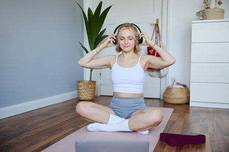 Portrait of fit and healthy young woman in wireless headphones, does workout, using online video tutorials, listens to fitness instructor on laptop, exercising at homeの写真素材