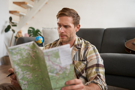 Portrait of man, traveller looks confused at map, studying the route to go on vacation or business tripの写真素材