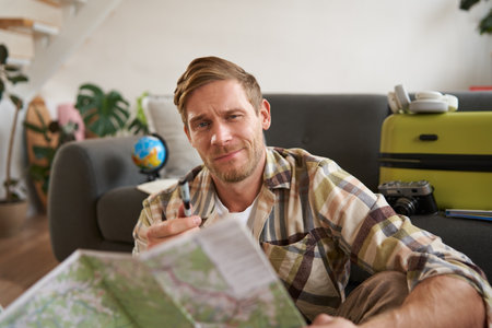 Smiling handsome man, traveller going on holiday, holding road map, planning his holiday, choosing the routeの写真素材