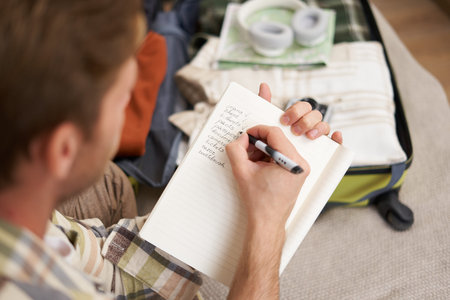 Close up portrait of man packing suitcase, making notes, check-list of items he wants to take on...