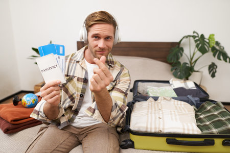 Image of handsome young man, tourist shows two plane tickets and passport, travels on holiday, goes on vacation, packs suitcasesの写真素材