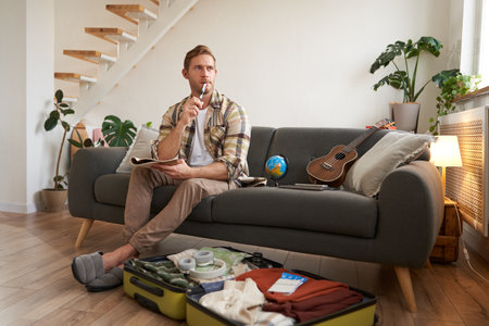 Portrait of young man packing for a trip, going on vacation, putting clothes inside suitcase, preparing for holidayの写真素材