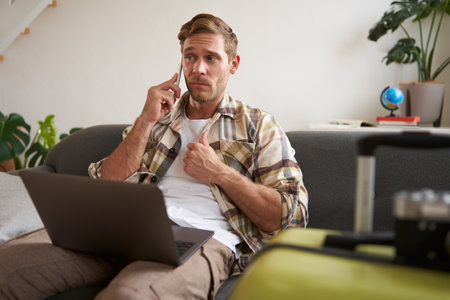 Portrait of man talking on mobile phone, tourist with laptop and suitcase answers telephoneの写真素材