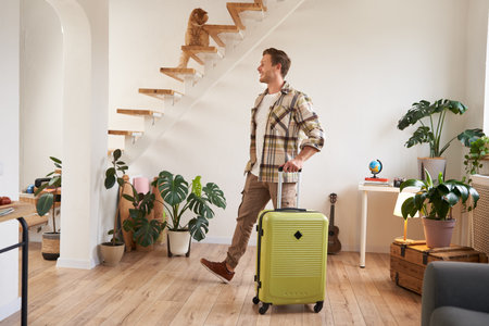 Portrait of handsome young man walking with suitcase in house, renting a room on vacation, smiling and looking happyの写真素材