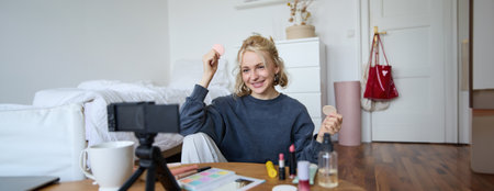 Portrait of young woman, beauty content creator, sitting in a room in front of digital camera, recording makeup tutorial vlog, showing cosmetic facial productsの写真素材