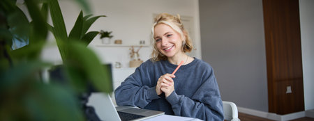 Portrait of young smiling woman, student talking to teacher online via video chat, doing course, attends remote course in internet, making notesの写真素材