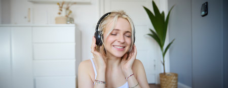 Concept of people and lifestyle, Close up of beautiful blond woman in wireless headphones, listens to music, enjoys good quality sound in new earphonesの写真素材