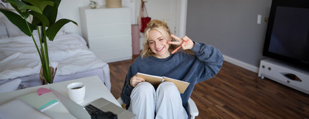 Portrait of smiling cute woman, lifestyle blogger, sits in her room with daily journal or planner, records video on digital camera, creates content for social media about daily routineの写真素材