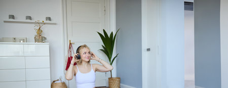 Vertical shot of smiling young woman using video tutorials for workout at home, sitting with laptop in wireless headphones on yoga mat, follows fitness instructor on social media, repeats exercisesの写真素材
