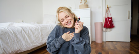 Portrait of young content creator, woman with social media account, recording video about makeup on digital camera, holding favorite lipstick, recommending product to audience onlineの写真素材