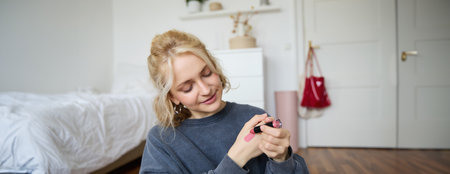 Portrait of young makeup artist, beauty blogger showing new lipstick, recording video in her room, smiling and expressing positivityの写真素材