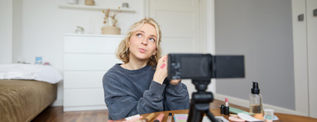 Portrait of young creative social media content creator, woman showing lipstick swatches on her hand, recording video about beauty and makeup, sitting in her room in front of digital cameraの写真素材