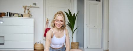 Vertical shot of woman recording her workout on digital camera, making a video about yoga and fitness at home, sitting on rubber mat in activewearの写真素材