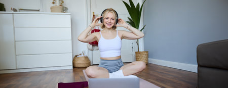 Portrait of fit and healthy young woman in wireless headphones, does workout, using online video tutorials, listens to fitness instructor on laptop, exercising at homeの写真素材