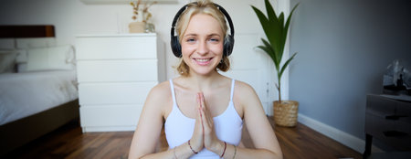 Wellbeing and people concept. Close up portrait of young woman in headphones, meditating, practice yoga, listens to podcast in earphonesの写真素材