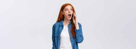 Girl hears amazing great news on phone. Excited lucky redhead girl pick-up phone realises she won challenge, gasping amazed and astonished, holding smartphone near ear, popping eyes surprisedの写真素材
