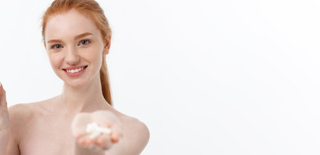 Portrait of good-looking young caucasian woman holding pills, trying to take care of immune system and health over gray background.の写真素材