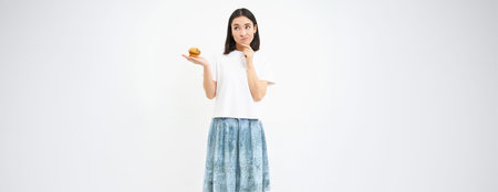 Woman with pensive face, holding cupcake and thinking, white background