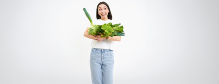 Portrait of smiling korean woman, hugs her vegetables, likes eating raw food, vegetarian enjoys nutritious diet, white backgroundの写真素材